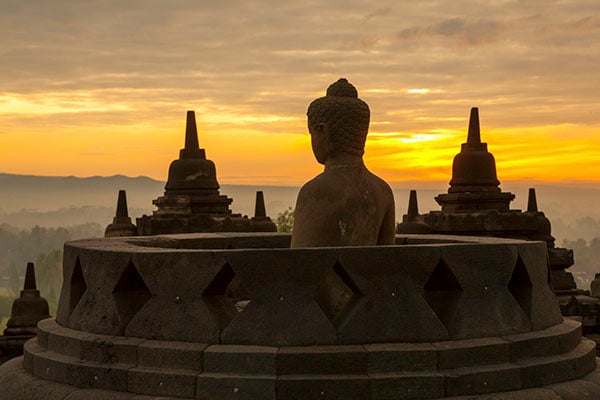 A silhouette of a buddha statue against a sunset.