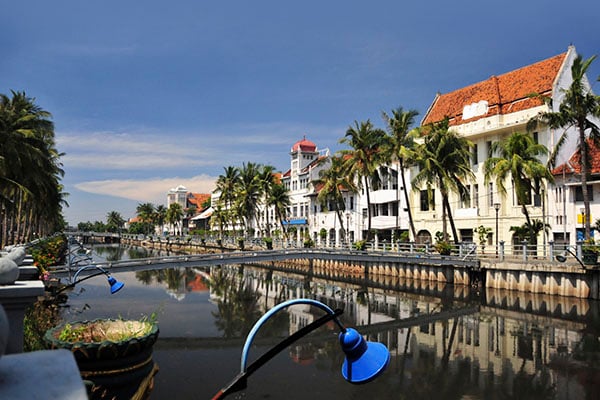 One of the many canals in Indonesia, lined by houses and palm trees.